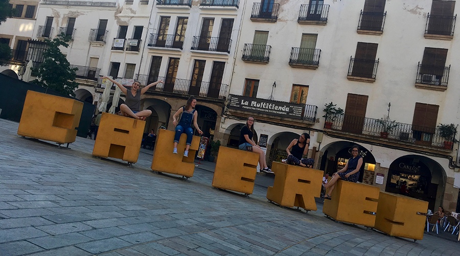 Students sitting on top of very large wood carved yellow block letters spelling Caceres 